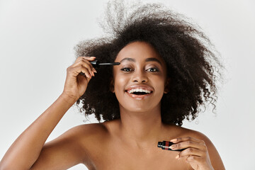 Obraz premium A beautiful young African American woman with her curly hair in a studio setting, applying mascara