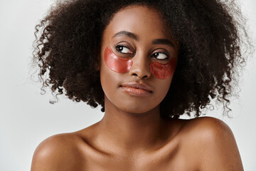 A beautiful young African American woman with curly hair wearing a striking red eye patch in a studio setting.