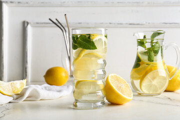 Glass and jug of fresh lemonade with mint on white background