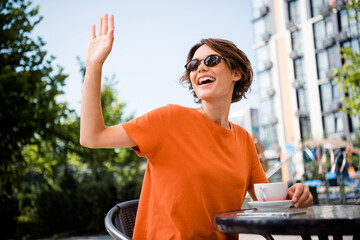 Photo of positive lovely girl dressed stylish outfit sitting in cafe drinking morning beverage meeting best friend saying hi © deagreez
