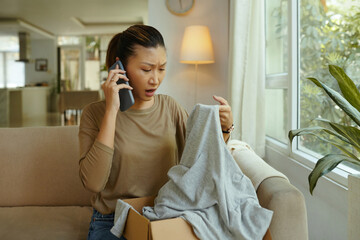 Upset customer making phone call about her defective order while sitting on sofa in the living room