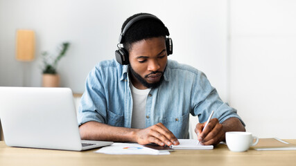 Concentrated african american guy in headphones studying foreign language online through video...