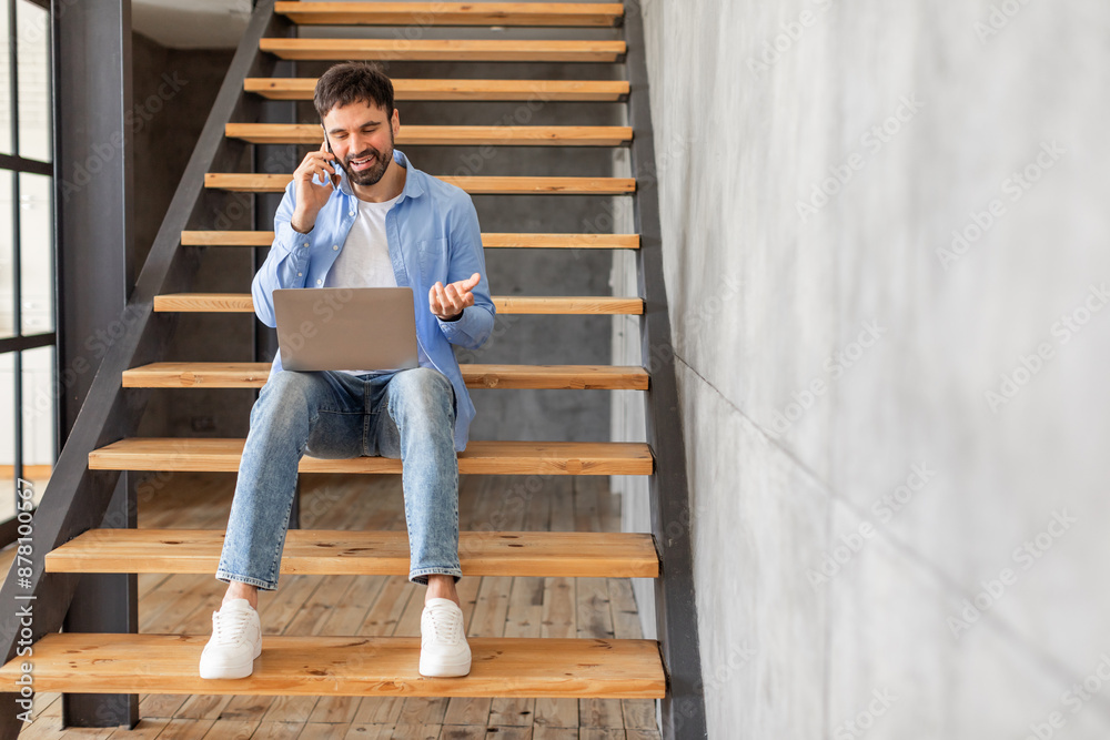 Poster this image shows a man sitting on a wooden staircase in a modern home, talking on a phone and using 