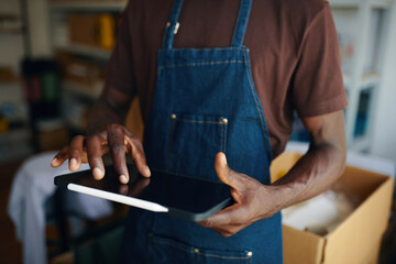 Obraz premium Close-up of worker checking online orders on tablet pc while working in warehouse