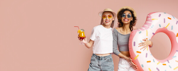 This image shows two happy friends posing with a donut pool float on a pink background. Both are smiling and wearing sunglasses. This image is perfect for representing summertime fun and friendship.