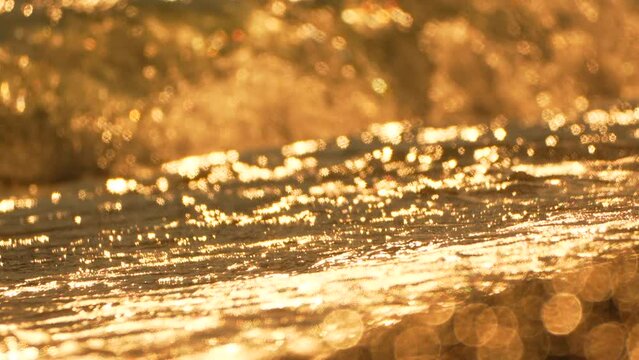 Golden sunset on the beach. Foamy waves rolling towards golden sand beach under low warm sun light. Slow motion. Nobody. Holiday recreation concept. Abstract nautical summer ocean sunset nature.