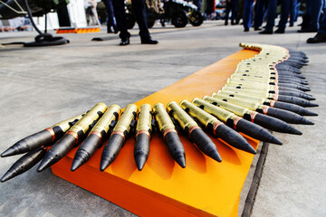 Obraz premium A close-up photo of a machine gun ammunition belt laying flat on an orange surface. The ammunition is a row of bullets with brass casings and black tips