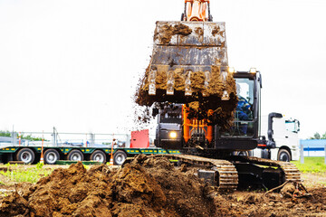 A black excavator digs dirt at a construction site, the bucket full of loose earth and soil