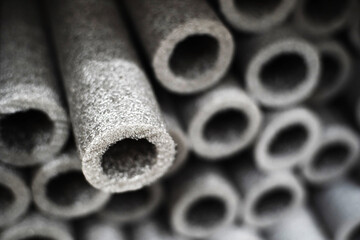 A close-up image of a stack of gray foam pipe insulation, with the texture of the foam and the circular shape of the pipes in focus