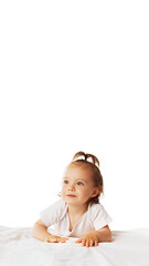 Vertical image of adorable little girl, baby in bodysuit, with ponytail leaning on bed and looking isolated on white background. Concept of childhood, care, health, infancy, lifestyle, motherhood