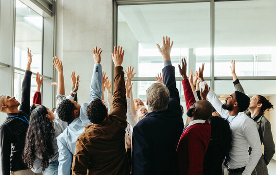 Excited business team raising hands at seminar in modern office building