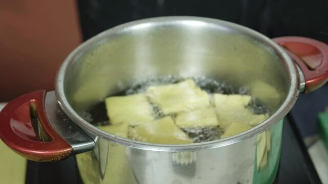 Chef taps wire mesh strainer on side of pot with boiling oil frying panelle