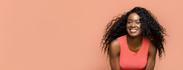 A young African American woman with long, curly black hair smiles brightly in front of a...