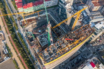 Aerial perspective of urban construction site with cranes, surrounded by buildings and streets in bustling city area