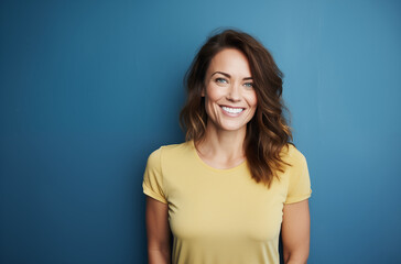 A happy woman wearing a yellow shirt, standing against a blue background and smiling warmly