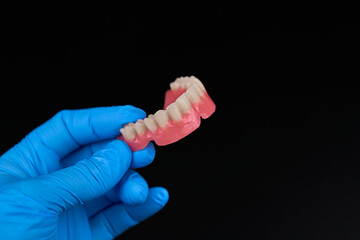 A person has blue gloves on and is holding a denture in their hand