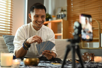 Tarot reader predicting online or recording video for blog with smartphone and ring light in foreground