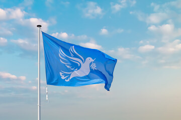 Waving blue peace flag with white dove holding an olive branch.in front of a moody blue sky