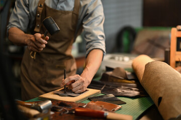 Cropped shot male artisan punching holes in leather piece. Small business and handmade concept