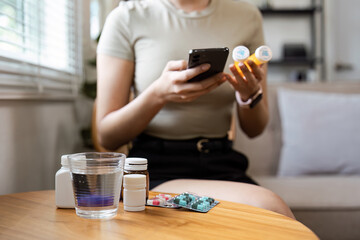 Woman Checking Medication Information on Smartphone While Holding Pill Bottles at Home