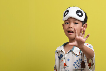 Portrait of Asian child wearing pajamas and sleeping mask isolated on yellow background. Child...