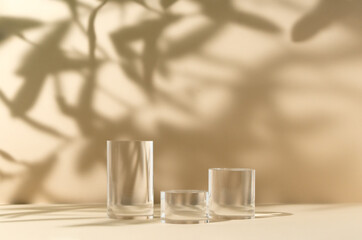 Capture elegance with this serene photo of three transparent glass cylinders on a beige background. Light and shadows create a tranquil, stylish scene, perfect for cosmetic products presentation.