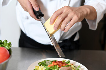 厨房でグレーターでチーズを削る調理師の手元