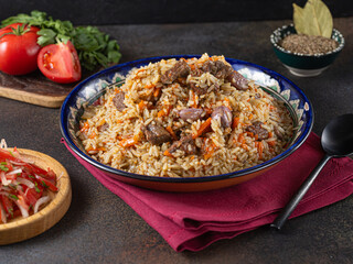 Pilaf, a dish of rice, chicken, carrots with spices and dried cranberries on a black plate on a dark wooden background. Eastern cuisine.