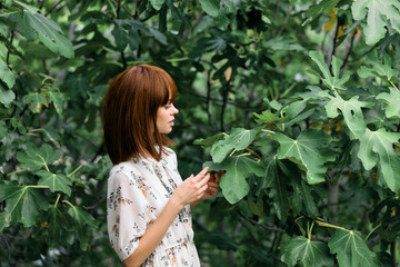 Woman standing by tree, examining ground below with curiosity and intrigue on a sunny day