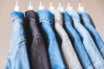 Many jean jackets on hangers, close-up view. Different shades of denim fabric colors.
