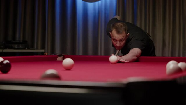 Billiards player in a trendy nightclub aims for the ball, strikes it, and misses the target pocket. Mid shot. Slow motion