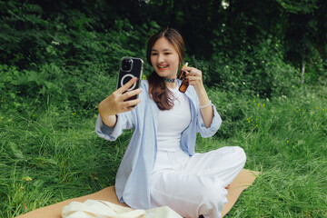 Korean girl with vial with essential oil in the park. Girl influencer advises her subscribers on...