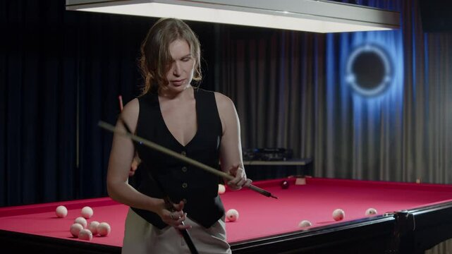 Woman is disassembling a cue at the end of a game, standing in front of an unusual red pool table in a nightclub. Mid shot. Slow motion