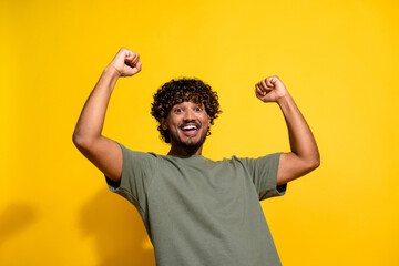 Fototapeta premium Photo of overjoyed guy with wavy hair dressed khaki t-shirt scream yeah raising fists up win bet isolated on yellow color background