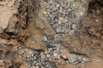 Top view on Calm transparent water surface, above view of underwater pebble. Clear crystal blue sea water and rocky, stone seabed background, texture.