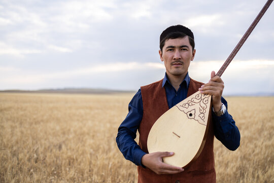 Kazakh, a man in Kazakh national dress playing dombra in the steppe. Kazakhstan. Central Asia. Nomads. | Казах, мужчина в казахской национальной одежде играет на домбре в степи. Казахстан.Средняя Азия