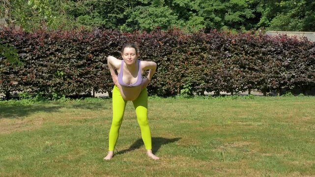 Pregnant caucasian woman bending over to stretch in the garden