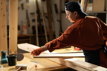 Attractive female carpenter measuring a wooden board working in her wooden workshop.