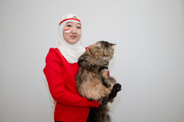 Woman in white hijab wearing red sweater. celebrating Indonesia's independence day. holding the tabby cat with excitement. isolation on white background.