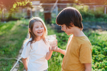 Obraz premium A boy and a girl hold a glass of water in their hands on a sunny day. Healthy lifestyle concept