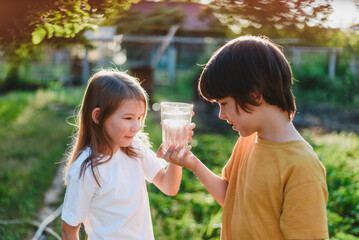 Obraz premium Beautiful children hold a glass of water in their hands in nature. Healthy lifestyle concept