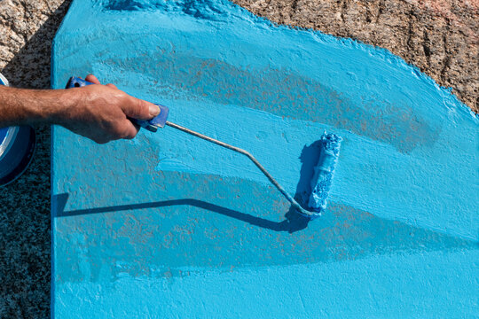 Pintor a pintar o ch&atilde;o de uma piscina com o seu pequeno rolo