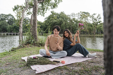 Young Couple Enjoying a Relaxing Picnic by the Lake with Flowers and a Book on a Beautiful Day in Nature