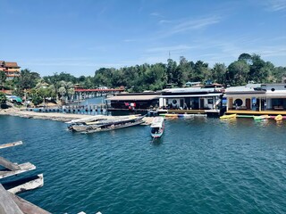 boats in the harbor
The image captures a scenic waterfront scene. A body of water, possibly a lake or river, stretches across the frame. Clear blue skies hover above, and lush greenery forms the backd