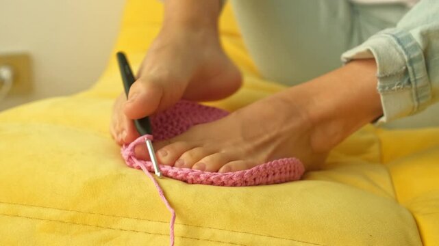 disabled woman using the foot to catch a hook to crochet, closeup female feets knitting interior decor basket usepink ribbon yarn and crochet hook.hobby or art work