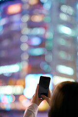 夜の繁華街でスマートフォンをかざす若い女性