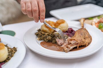 Person Using Fork to Eat Roast Duck With Sides of Dumplings, Red Cabbage, and Gravy on White Plate