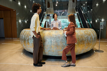 Three colleagues converse in a modern office lobby, one woman with a prosthetic leg.