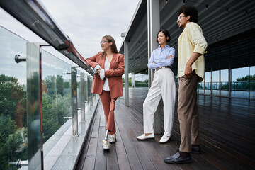 Three colleagues, including one with a prosthetic leg, chat and laugh on a modern office rooftop...
