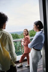 Three colleagues chat on a modern office rooftop terrace, enjoying the view.